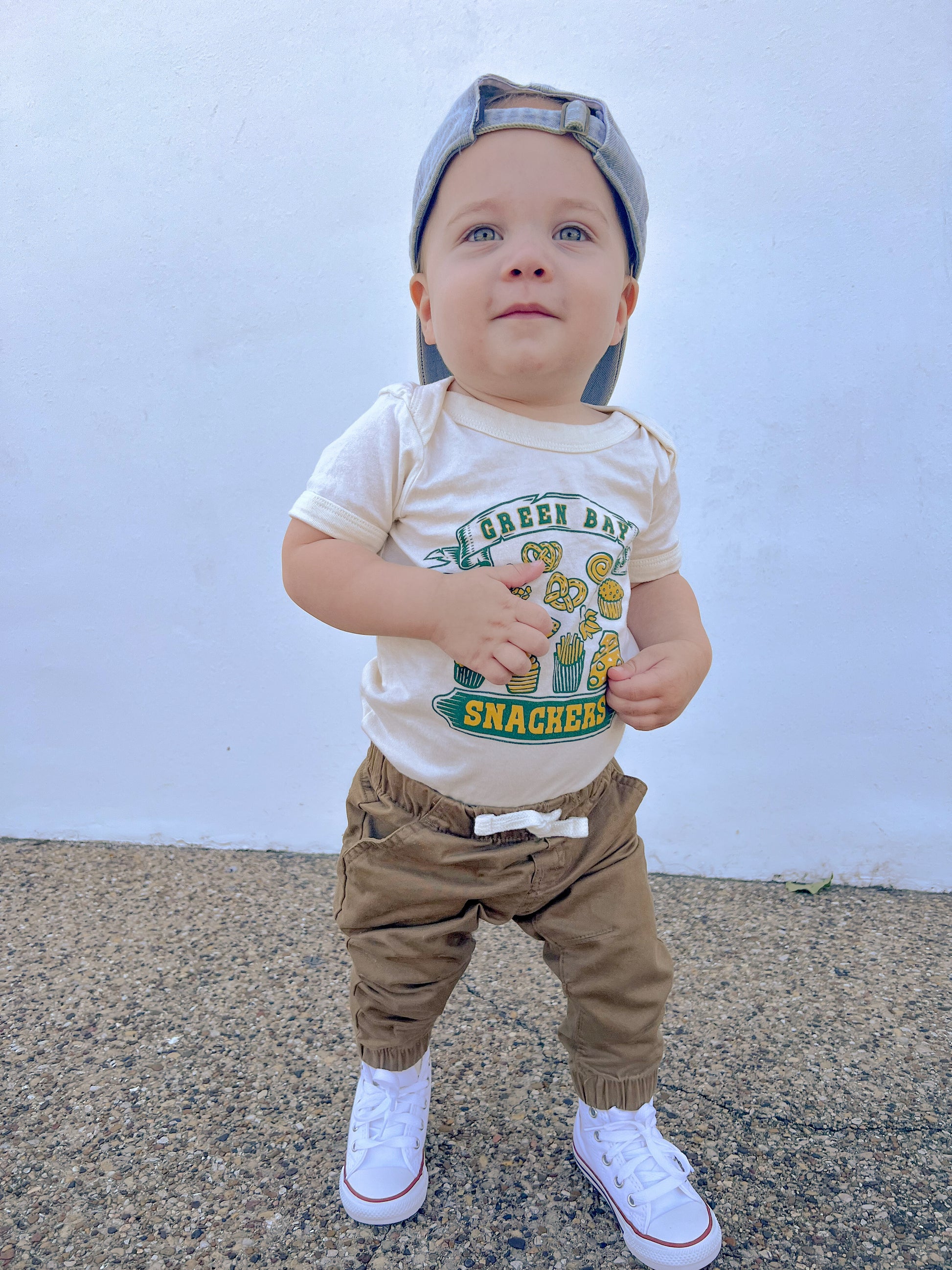 Child wearing a 'Green Bay Snackers' shirt with a plain background